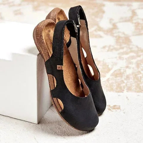 Black leather slingback flats with cut-out side detail and tan cushioned footbed, shown from above and side on a white box.