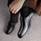 Overhead view of black leather slip-on shoes being worn, highlighting the textured upper and segmented rubber outsole
