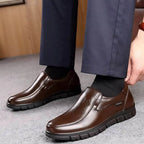 Close-up of brown leather slip-on shoes worn with navy trousers, with a hand adjusting the heel for a snug fit
