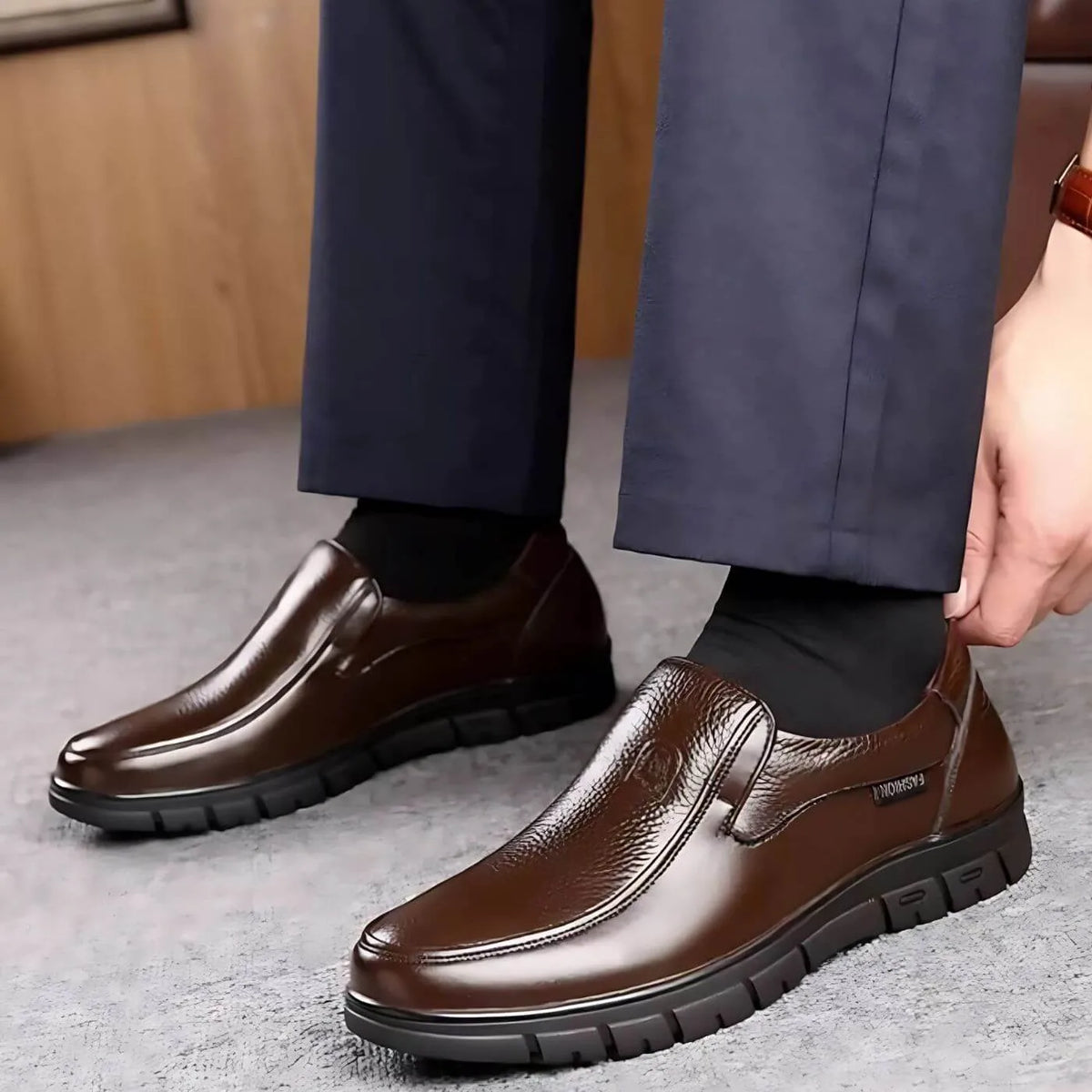 Close-up of brown leather slip-on shoes worn with navy trousers, with a hand adjusting the heel for a snug fit