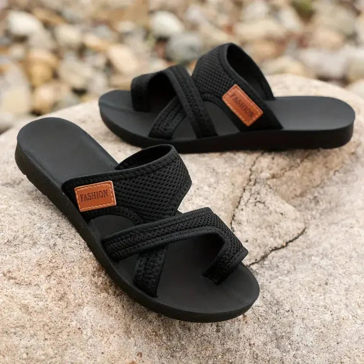 Pair of black mesh crisscross sandals placed on a rock, showing matching chunky soles from the side