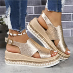 Close-up side view of gold crocodile-embossed platform wedge sandals with woven espadrille trim and buckle strap