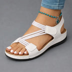 White elasticised crisscross sandal with woven straps and tan insole, worn with a turquoise beaded anklet.