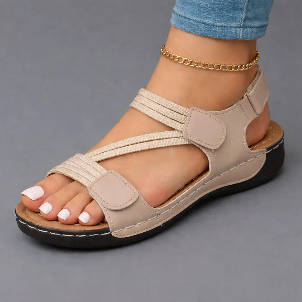 Beige faux leather strappy sandal with elastic straps and visible stitched sole detail, shown on a model's foot.