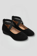 Pair of black suede ballet flats with crisscross elastic ankle straps and a low wedge heel, shown at an angle