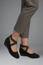 Side view showing the low wedge sole and elastic crisscross straps of black suede flats on foot