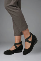 Close-up side profile of black suede wedge flats with elastic ankle straps and rounded toe