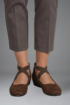 Front view of brown suede ballet flats with crisscross elastic straps worn with grey cropped trousers