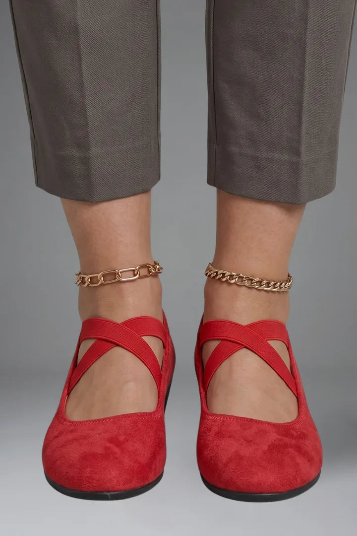 Front view of red suede ballet flats with crisscross elastic straps, paired with gold ankle chains