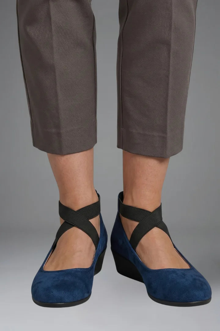 Close-up of black suede flats on foot highlighting the textured sole and elastic strap detail