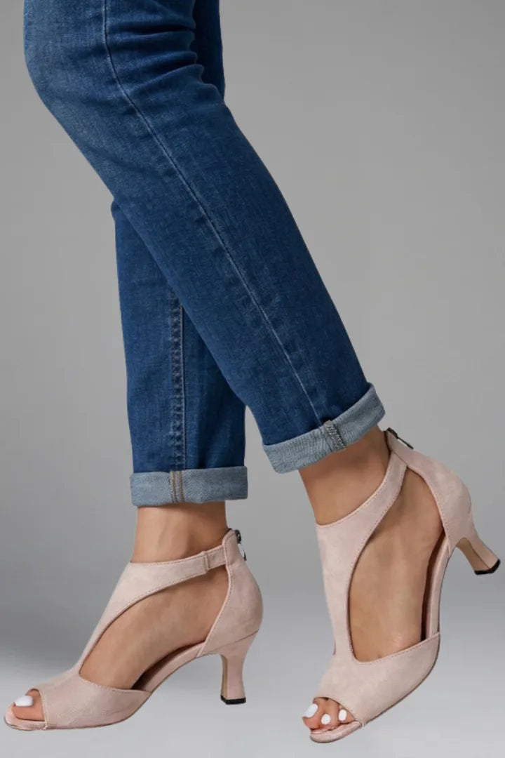 Side view of pink suede cutout heels with a mid height heel, worn with rolled-up jeans