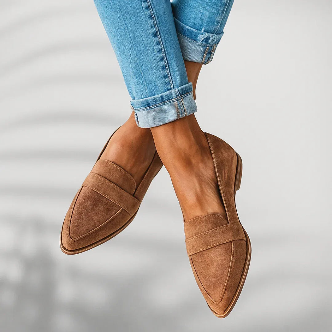 Side angle of tan suede penny loafers with crossed ankles, paired with rolled light-wash denim