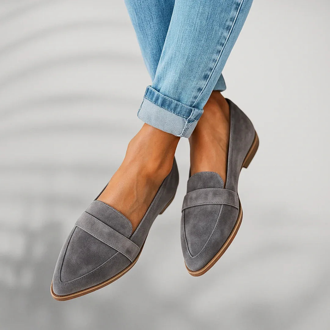 Close-up front view of grey suede loafers with penny-keeper strap and tan sole detail