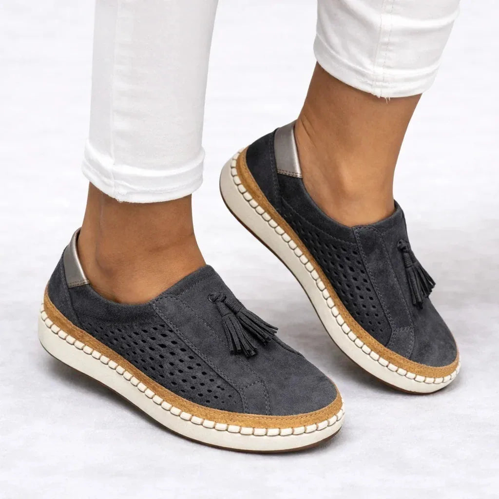 Charcoal grey suede slip-on sneakers worn with cuffed white jeans, showing perforated cutouts and the contrast cork and white sole