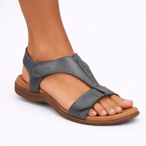 Grey T-strap sandal shown on foot, featuring stitched straps and a padded contoured sole