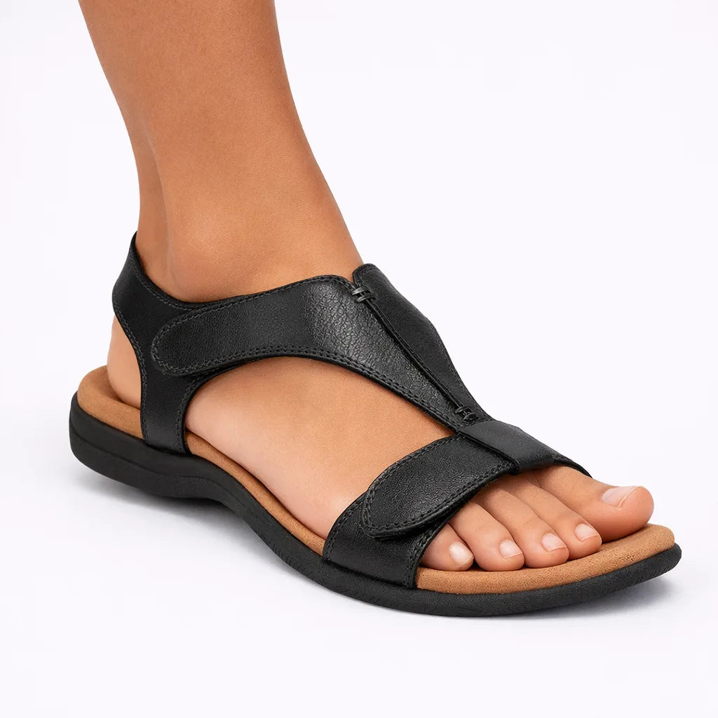 Black T-strap sandal with hook-and-loop closure and low stable sole, worn on a model's foot