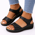 Black two-strap wedge sandal with contrast stitching and open toe, worn with rolled denim jeans