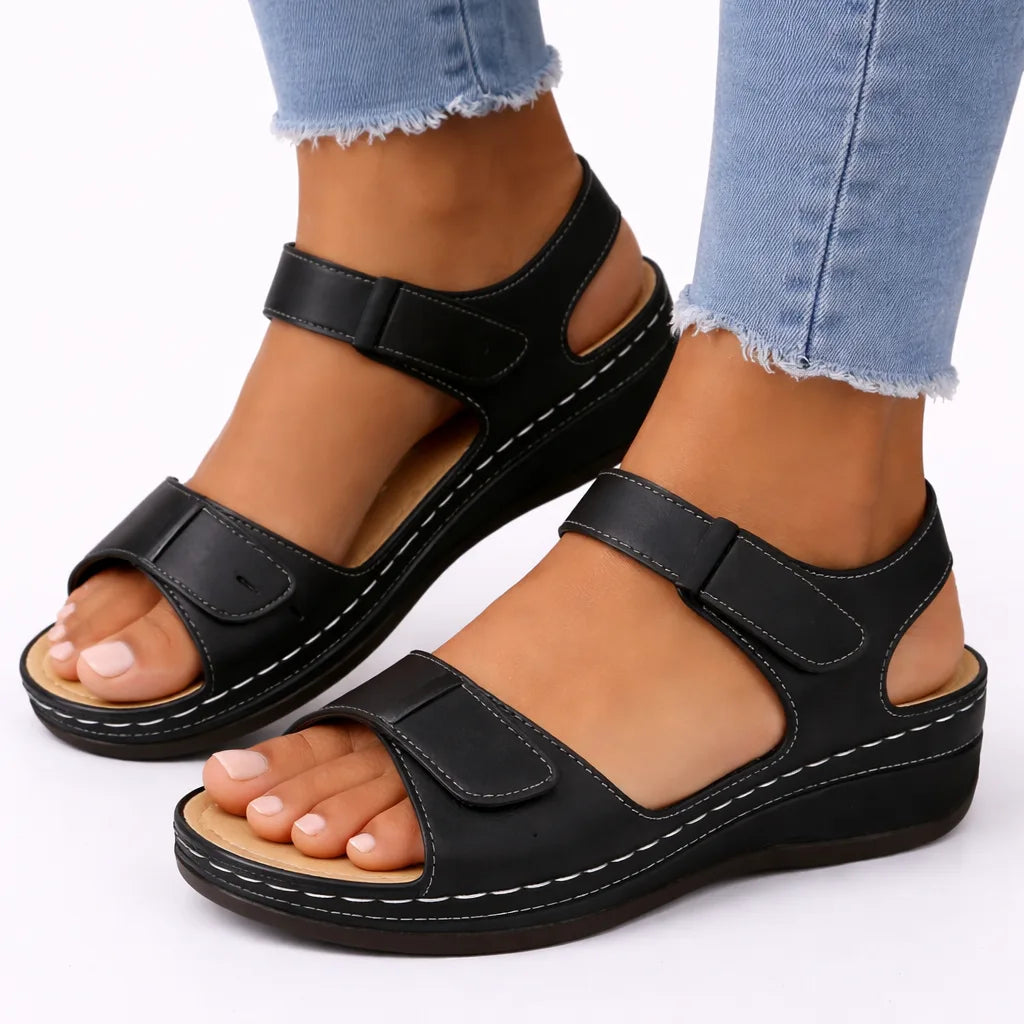 Black two-strap wedge sandal with contrast stitching and open toe, worn with rolled denim jeans