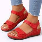 Red double-strap wedge sandal with cream stitching and adjustable touch-fasten straps, on foot