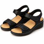 Studio pair shot of black wedge sandals showing tan cushioned footbed and stitched outsole detail