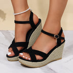 Close-up side view of black suede crisscross wedge sandals with espadrille platform and pearl anklet styling