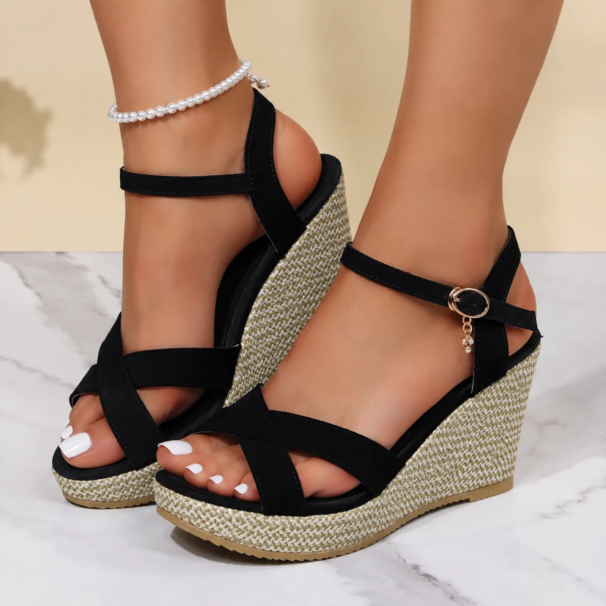Close-up side view of black suede crisscross wedge sandals with espadrille platform and pearl anklet styling
