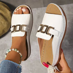 Overhead pair shot of white slide sandals resting on a grey surface, highlighting the thick tan midsole and stitched edges