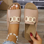 Top view of nude beige slide sandals on a wooden surface, showing the open toe front and gold buckle hardware