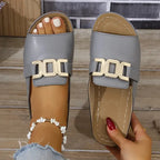 Top view of grey slide sandals on a wooden step, showing the rounded open toe and metallic gold buckle trim