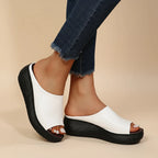 Side view of white faux leather peg-toe wedge slide with thick black platform sole, worn with cropped jeans