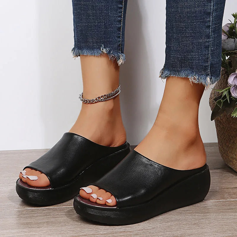 Close-up of black peep-toe wedge slide showing pebbled faux leather texture and chunky heel