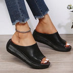 Outdoor-style shot of white wedge slides with textured black platform sole against wood flooring