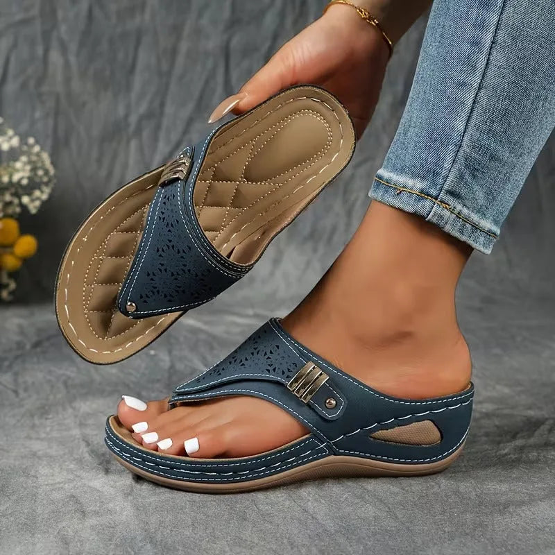 Side view of blue flip-toe wedge sandal with perforated floral cut-outs and cushioned tan footbed held in hand