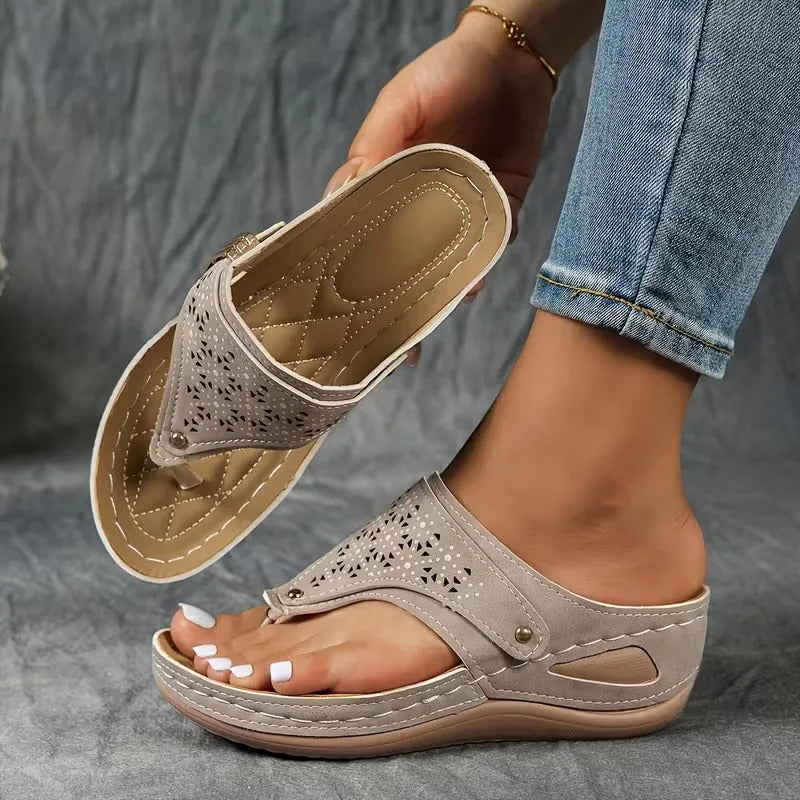 Black wedge sandal worn on foot, showing toe-post design, metal buckle trim and stitched wedge sole