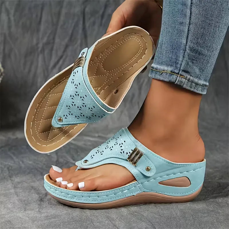 Purple wedge sandal with floral laser-cut upper and quilted tan footbed, shown held beside bare foot