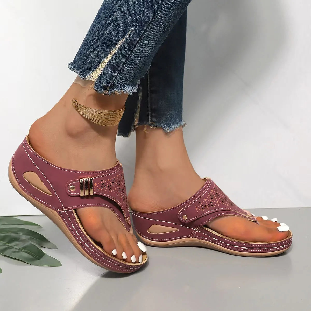 Brown wedge sandal with perforated toe strap and padded insole, displayed against grey fabric backdrop