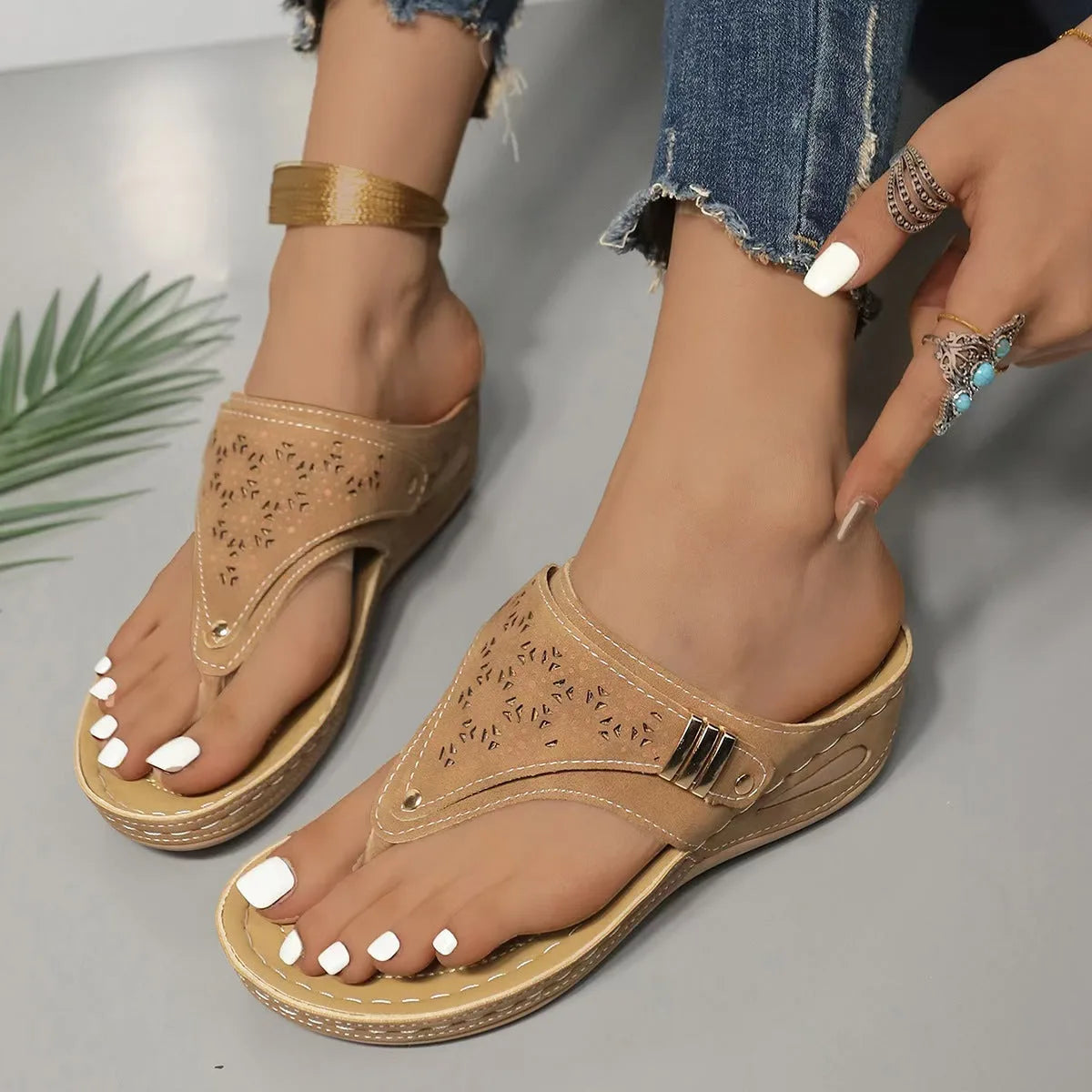 Close-up side angle of navy blue toe-post wedge sandals worn on feet with white pedicure and ankle bracelet