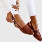Hand adjusting the buckle on a brown woven leather slingback flat for a secure fit