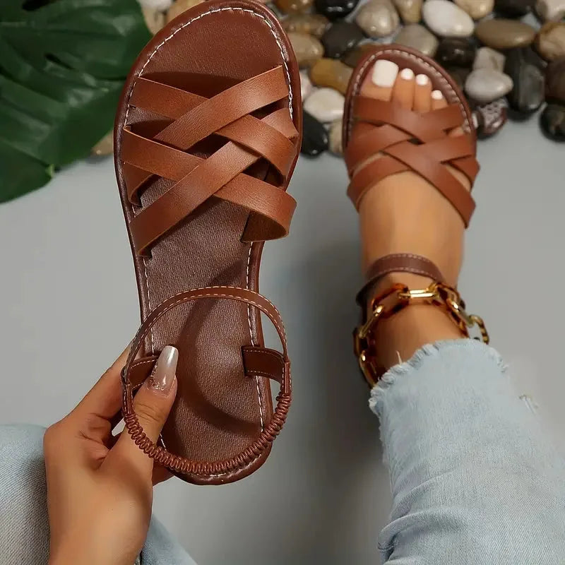 Close-up top view of brown crisscross sandal strap and elastic heel strap held in hand beside a worn sandal