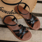 Pair of brown crisscross strap flat sandals resting on a woven straw placemat with small white flowers