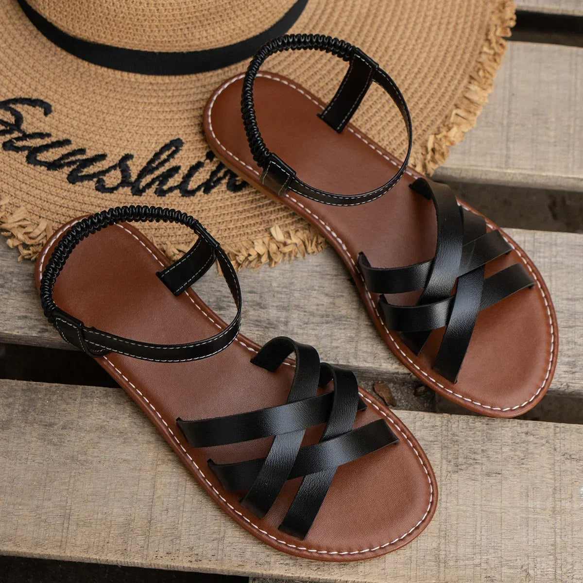Pair of brown crisscross strap flat sandals resting on a woven straw placemat with small white flowers