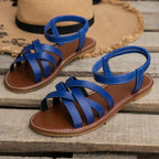 Close-up top view of white crisscross sandal strap held in hand next to a worn white sandal on straw mat