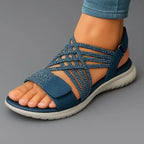Close-up side view of blue woven strappy sandal with white cushioned sole worn on foot, paired with rolled denim