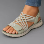 Sage green crisscross strap sandal with knit-texture upper and white sneaker-style sole shown on model's foot