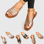 Gold strappy flat sandals with a woven square-toe design, worn on foot and paired with a gold anklet.