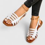 White woven strappy flat sandals with square open toe, shown worn with a gold ankle chain.