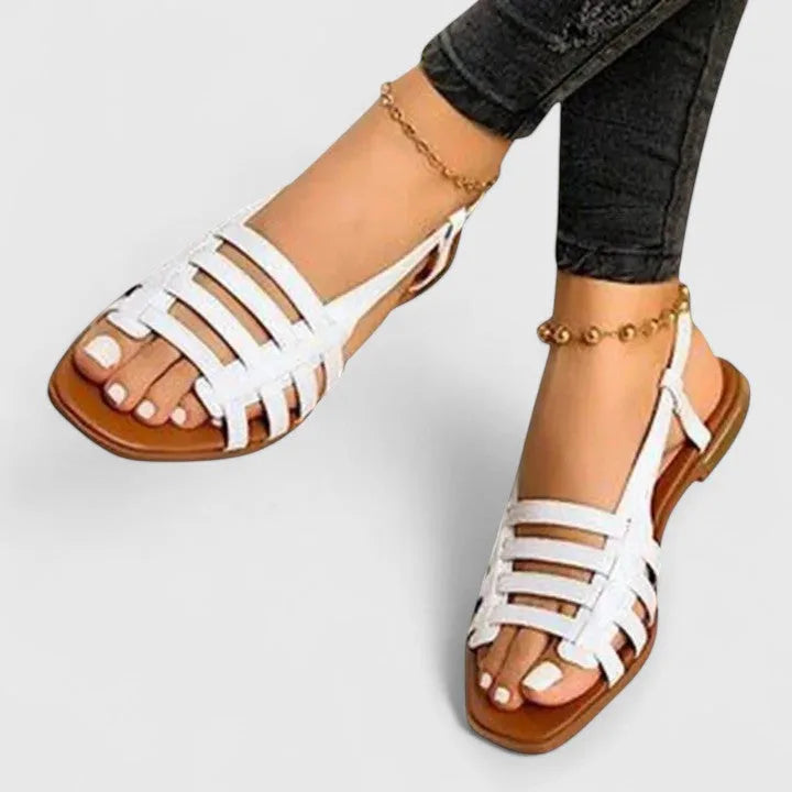 White woven strappy flat sandals with square open toe, shown worn with a gold ankle chain.