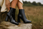 Close up of black patent ankle boots worn outdoors with a cream sweater, showing the pointed toe.