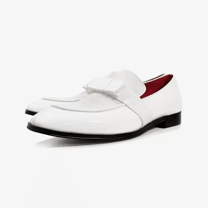Three-quarter view of white patent leather loafers with matching bow detail and black sole