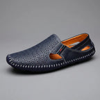 Side profile of a single navy perforated leather loafer with tan interior and whipstitched sole on grey background